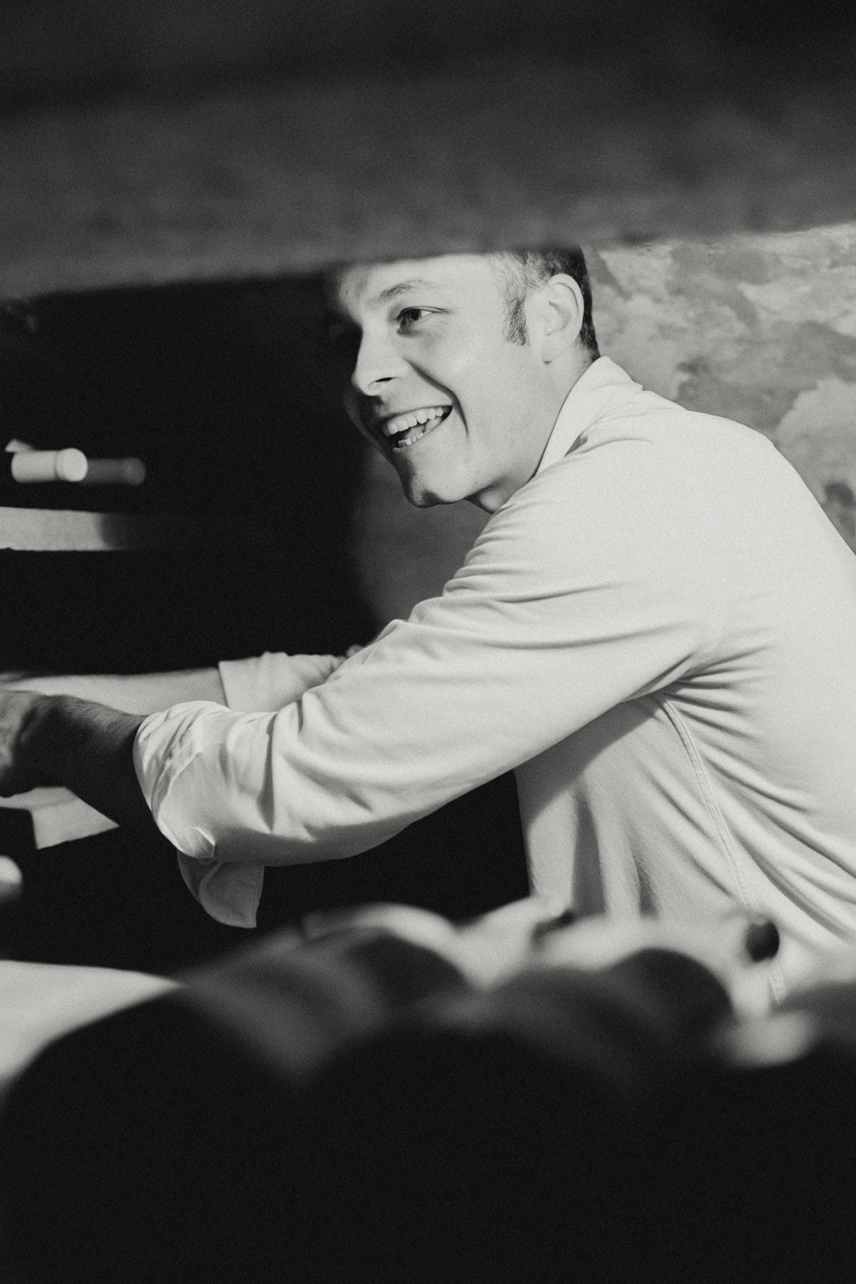Martijn, sommelier van Nyde, met een glimlach, gekleed in een wit shirt, buigt zich over een tafel in een donkere ruimte terwijl hij bezig is met het uitkiezen van wijn.