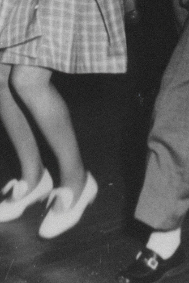 Een zwart-wit afbeelding van dansende voeten, met een focus op een paar lichte schoenen aan de linkerkant en een paar donkere schoenen aan de rechterkant.