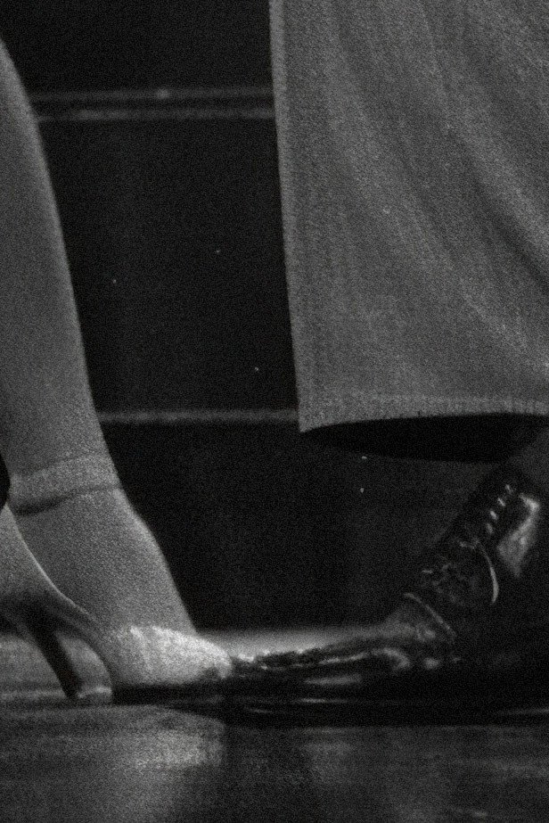Een close-up van een dames- en herenvoet tijdens het dansen, in zwart-wit.